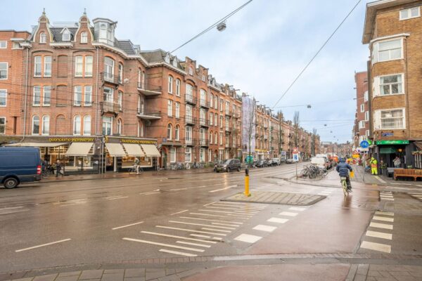 Straatbeeld van de Admiraal de Ruijterweg in Amsterdam met karakteristieke bakstenen panden, winkels en fietsers.